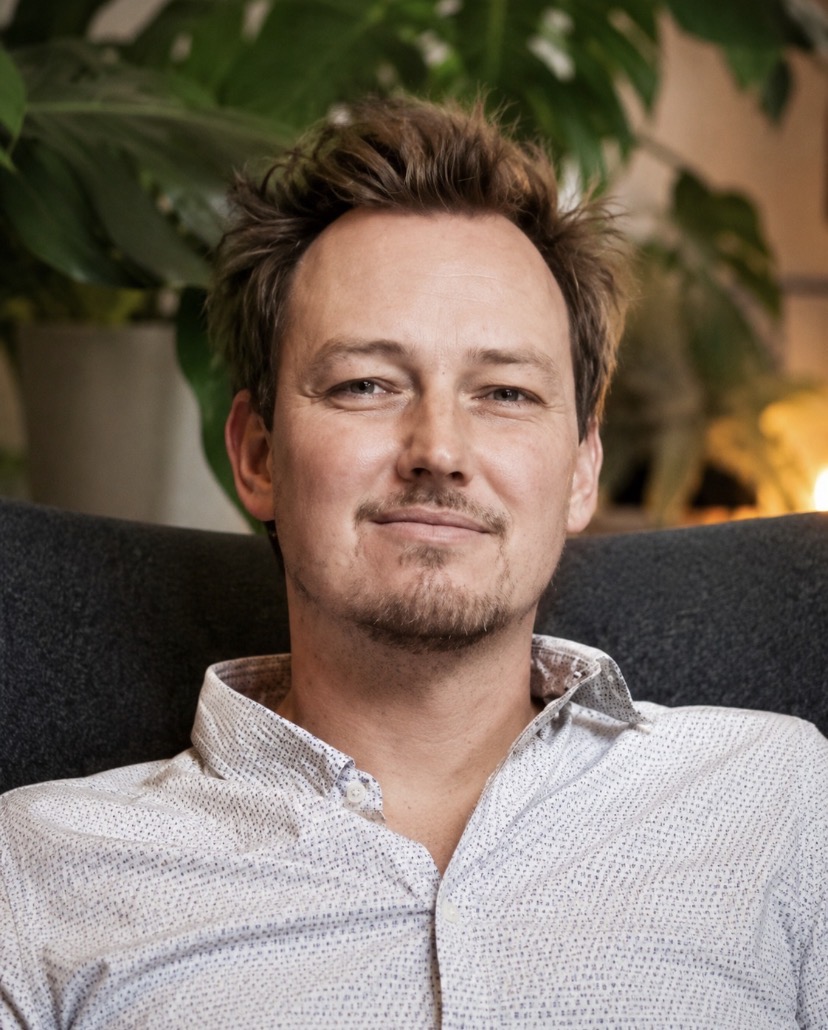 Lukas Blaik, Heilpraktiker für Psychotherapie und Coach, sitzt entspannt auf einem Sofa vor Pflanzen und lächelt leicht